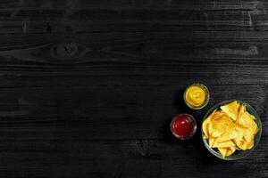 Snack zum Party, Chips, Nachos mit Saucen Tomate Ketchup , Senf auf ein schwarz Hintergrund. oben Sicht, Kopieren Raum foto