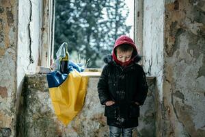 wenig Junge im ein ruiniert Haus Krieg im Ukraine ukrainisch Flagge foto