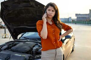 Frau steht in der Nähe von das Auto im welche das Motor werden nicht Start. Stehen in der Nähe von das gebrochen Auto Berufung zum Auto Reparatur Bedienung foto