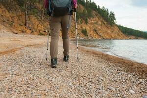 Wandern Tourismus Abenteuer. unkenntlich Wanderer Mädchen Tourist mit Rucksack Gehen in der Nähe von See. Backpacker Frau Füße und schön Strand Sicht, zurück Aussicht Frau genießen Wanderung Trekking Tourismus aktiv Ferien foto