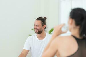 jung weiblich und männlich Sportler Sitzung sich ausruhen auf Yoga Matten und Trinken Wasser. Sie sind suchen beim jeder andere und lächelnd foto