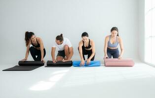 ein Gruppe von weiblich und männlich Sportler tun Yoga Aktivitäten beim Studio, rollen oben das Yoga Matte foto