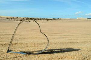 ein Herz geformt Metall Objekt im das Sand foto