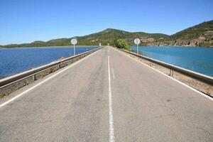 ein lange leeren Straße mit ein Brücke Über ein See foto