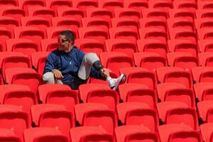 deaktiviert Sportler im ein Blau Hemd Sitzung auf das rot Sitze beim das Stadion, bereiten zum Laufen Ausbildung. foto