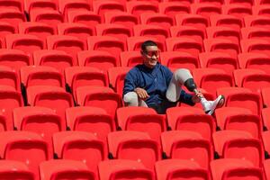 deaktiviert Sportler im ein Blau Hemd Sitzung auf das rot Sitze beim das Stadion, bereiten zum Laufen Ausbildung. foto