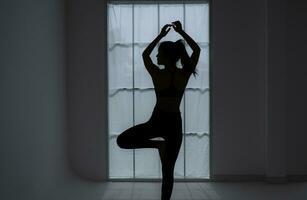 Silhouette von ein jung Frau üben Yoga im das Zimmer. foto