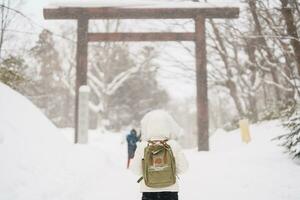 Frau Tourist Besuch im sapporo, Reisender im Sweatshirt suchen Hokkaido Schrein mit Schnee im Winter Jahreszeit. Wahrzeichen und Beliebt zum Sehenswürdigkeiten im Hokkaido, Japan. Reise und Ferien Konzept foto