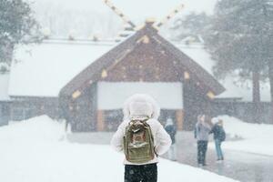 Frau Tourist Besuch im sapporo, Reisender im Sweatshirt suchen Hokkaido Schrein mit Schnee im Winter Jahreszeit. Wahrzeichen und Beliebt zum Sehenswürdigkeiten im Hokkaido, Japan. Reise und Ferien Konzept foto