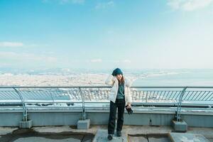 Frau Tourist Besuch im Hakodate, Reisender im Sweatshirt Besichtigung Aussicht von hakodate Berg mit Schnee im Winter. Wahrzeichen und Beliebt zum Sehenswürdigkeiten im Hokkaido, japan.reisen und Ferien Konzept foto