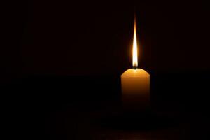 eine einzelne brennende Kerzenflamme oder ein Licht, das auf einer gelben Kerze leuchtet, die auf rotem oder dunklem Hintergrund auf dem Tisch in der Kirche für Weihnachten, Beerdigung oder Gedenkgottesdienst isoliert ist foto