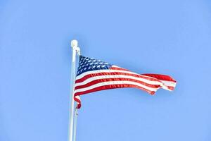 ein amerikanisch Flagge fliegend im das Wind gegen ein Blau Himmel foto