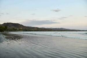 ein Strand mit Wellen und Berge im das Hintergrund foto