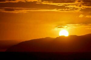 das Sonne setzt Über das Ozean und Berge foto