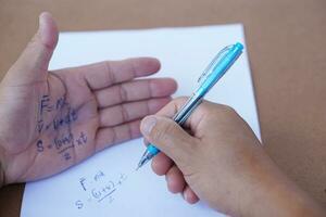 Palme mit geschrieben Physik Formel auf es während tun Schreiben Untersuchung auf Papier durch Stift. Konzept, betrügen das prüfen, unehrlich Verhalten. Bildung Bewertung. foto