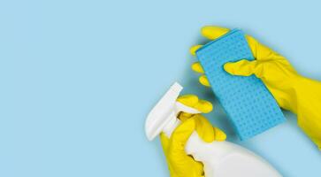 Hände im Gelb Gummi Handschuhe halt ein Reiniger sprühen und Lappen auf ein Blau Hintergrund. Reinigung Konzept. Banner. Nahansicht. oben Sicht. Platz zum Text. foto