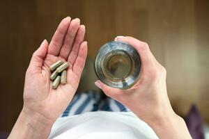 Frau hält Kräuter- Tabletten und Glas von Wasser im ihr Hände. nehmen Vitamine, Ergänzungen. Nahansicht. oben Sicht. selektiv Fokus. foto