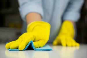 Hausfrau im Gelb Gummi Handschuhe Tücher das Küche Tabelle mit ein Lappen. Hauswirtschaft Konzept. Nahansicht. selektiv Fokus. foto