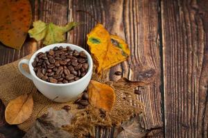 Tasse Kaffeebohnen und trockene Blätter auf Holzboden, Hallo September-Konzept. foto