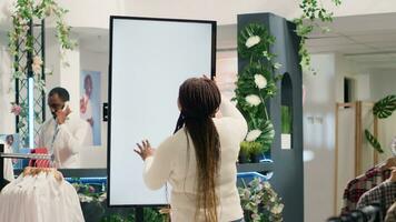 afrikanisch amerikanisch Frau im Mode Boutique mit Attrappe, Lehrmodell, Simulation erweitert Wirklichkeit Bildschirm zu aussehen beim Kleider Optionen zu Versuchen An. Kunde mit LED Kiosk zu visualisieren Outfit Kombinationen im Geschäft Vor Kauf foto