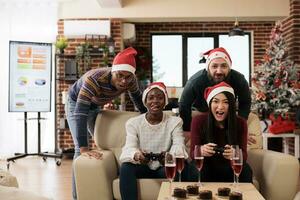 korporativ Mitarbeiter haben heiter Weihnachten Feier, spielen Video Spiel zusammen auf Sofa. Kollegen entspannend und Sitzung auf Couch mit Gamepads im festlich dekoriert Büro foto