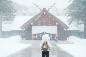 Frau Tourist Besuch im sapporo, Reisender im Sweatshirt suchen Hokkaido Schrein mit Schnee im Winter Jahreszeit. Wahrzeichen und Beliebt zum Sehenswürdigkeiten im Hokkaido, Japan. Reise und Ferien Konzept foto