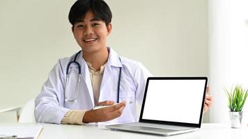 Facharzt in einem Laborkittel mit einem Stethoskop benutzt einen Laptop, um Patienten zu führen, der Arzt verwendet einen Laptop, um Online-Behandlungen zu empfehlen.