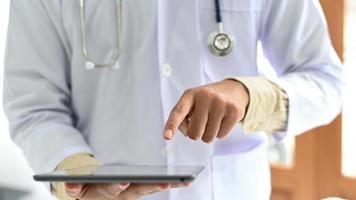 Nahaufnahme eines Arztes, der auf ein Tablet zeigt, ein Mann in einem medizinischen Kittel mit einem Stethoskop, der das Tablet bedient. foto