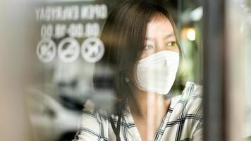 asiatische frau, die eine medizinische maske trägt und aus dem fenster eines cafés schaut. foto