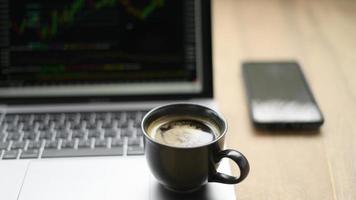Kaffeetasse auf Laptop mit Aktiendiagramm auf dem Bildschirm platziert, von vorne geschossen. foto