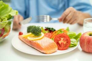 asiatisch Alten Frau geduldig Essen Lachs Steak Frühstück mit Gemüse gesund Essen im Krankenhaus. foto