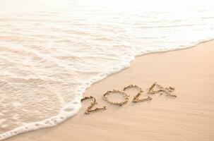 2024 Jahr geschrieben auf das Strand im das Sonnenuntergang Zeit. Neu Jahr 2024 Konzept foto