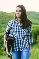 Mädchen Gehen im das Feld mit ein Gitarre im Hand foto