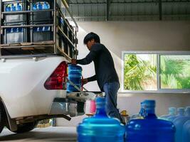 Arbeitskräfte Aufzug Trinken Wasser klar und sauber im Blau Plastik Gallone in das zurück von ein Transport LKW gereinigt Trinken Wasser Innerhalb das Produktion Linie klein Geschäft foto