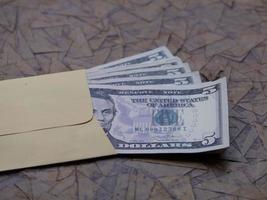 US-Dollar-Banknoten in gelbem Papierumschlag auf brauner Oberfläche