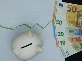 Europäische Banknoten und Sparschwein im Hintergrund mit ansteigender grüner Trendlinie, Ansicht von oben
