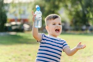 froh Kind Getränke klar Wasser von ein Flasche auf ein sonnig Tag im Natur foto