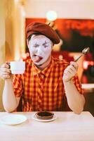 das Clown ist Essen ein Kuchen im ein Cafe und seine Gesicht ist krächzend. foto