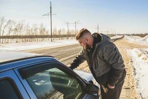 Mann steht in der Nähe von seine gebrochen Auto im Winter foto