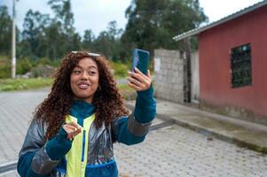 ziemlich Latina tausendjährig Mädchen reden auf ihr Zelle Telefon zu ihr Anhänger während zeigen ihr ländlich Abenteuer. Welt Influencer Tag foto