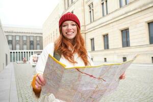 schön Rothaarige Frau, Tourist mit Stadt Karte, erforscht Besichtigung historisch Wahrzeichen, Gehen um alt Stadt, lächelnd glücklich foto