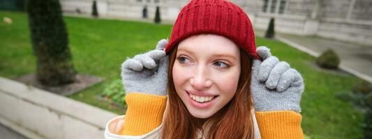 süß Mädchen Schüler im rot Hut, warm Handschuhe, sitzt im Park, lächelt und sieht aus glücklich. foto