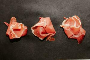 Stücke von getrocknet Schweinefleisch Jamon Prosciutto auf ein schwarz Tafel foto