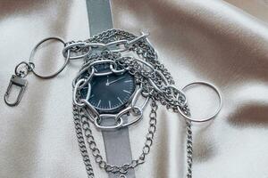 stilvoll Silber Kette Dekorationen zum das Hals und Uhr auf ein Seide glänzend Hintergrund. foto