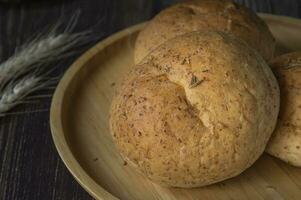 drei Rollen Brötchen auf ein hölzern Teller mit Weizen foto