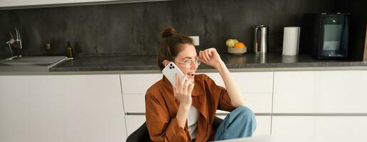 Bild von schön modern Frau Arbeiten von heim, studieren im Küche mit Laptop, reden auf Smartphone, Berufung jemand auf Telefon foto