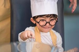 Porträt süßer kleiner asiatischer glücklicher Junge, der daran interessiert ist, mit Mutter lustig in der heimischen Küche zu kochen. Menschen Lebensstil und Familie. Konzept für hausgemachte Speisen und Zutaten. Weihnachtskuchen und Kekse backen foto