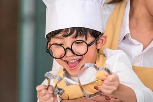 süßer kleiner asiatischer glücklicher Junge, der daran interessiert ist, mit Mutter lustig in der heimischen Küche zu kochen. Menschen Lebensstil und Familie. Konzept für hausgemachte Speisen und Zutaten. zwei Leute backen Weihnachtskuchen und Kekse foto