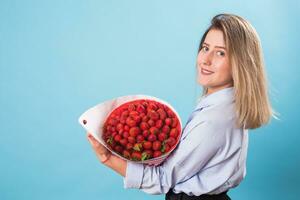 jung Frau halten Strauß von Erdbeeren auf Blau Hintergrund. foto