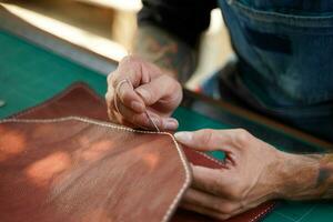 Nahansicht Hand von Leder Handwerker ist vorsichtig zu nähen ein Leder Tasche zum ein Kunde., Leder Handwerker Konzept. foto